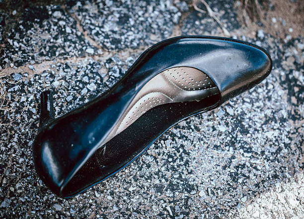 A lone black high heel rests on the sidewalk, separated from its pair and marked by the street. Its quiet presence hints at an untold story, inviting the viewer to wonder how it came to be left behind.