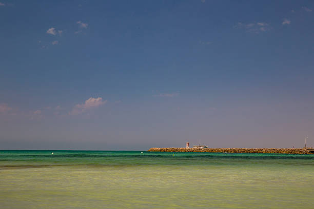 Peaceful breakwater with lighthouse, blue sky and calm sea.