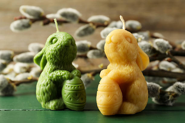 Colorful bunny-shaped candles and willow branches on green wooden table, closeup. Easter decor