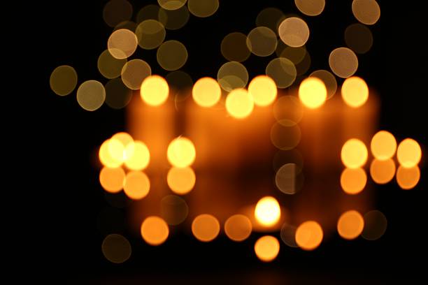 Blurred view of burning candles in darkness, bokeh effect