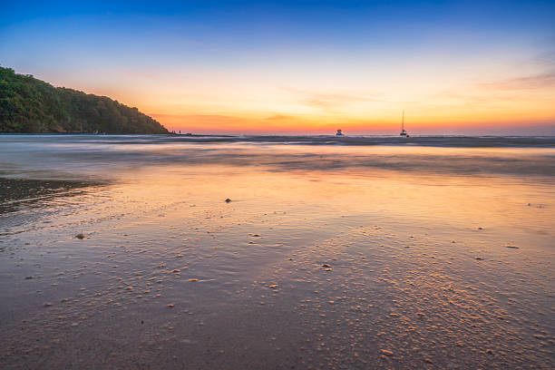 Beautiful tropical beach at sunset with golden light reflecting on the wet sand and calm waves under a vibrant twilight sky