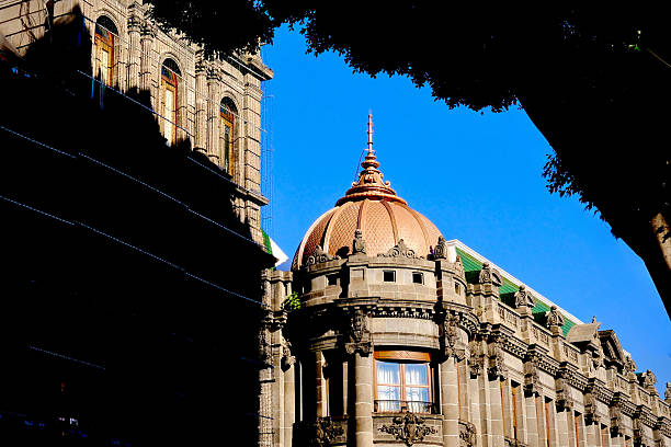 A copper dome crowns an ornate stone building framed by trees and strong afternoon light.