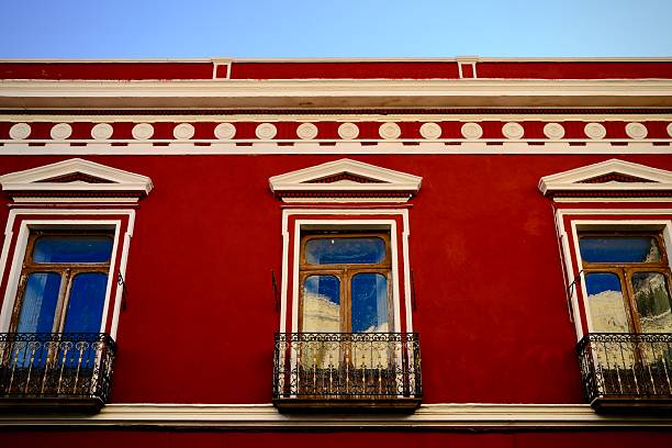 A red colonial facade features tall windows and iron balconies with decorative trim.