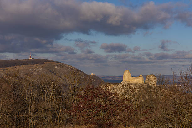 Ancient stone ruins overlook a vibrant valley with lush green hills and distant mountains under a warm sunset glow.