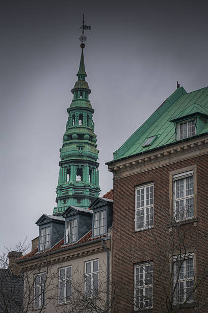 Green copper spire above Copenhagen rooftops under cloudy sky