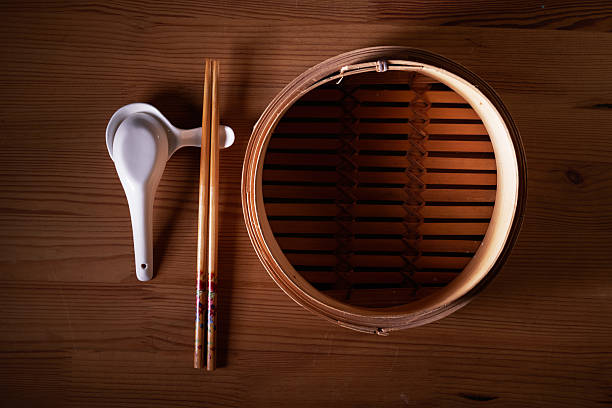 Bamboo steamer, chopsticks and ceramic spoon on wooden background