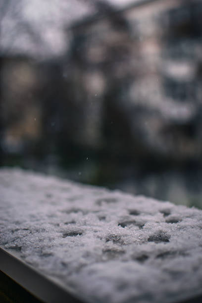 Close-up view of fresh snow resting on an urban surface with blurred background, creating a quiet, atmospheric scene that conveys winter, stillness, and the passage of time.