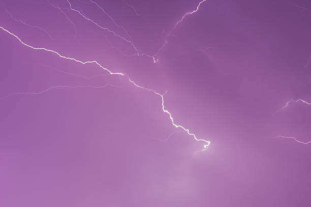 Close-up of a vivid lightning strike branching across a dramatic purple sky, highlighting the power and energy of a thunderstorm. The abstract composition emphasizes the electric lines and glowing clouds.