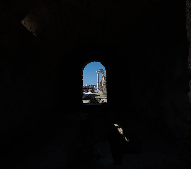 View of the Temple of Apollo columns in Side, Turkey, framed by a dark stone archway silhouette. Minimalist high-contrast composition with ample black negative space for text.