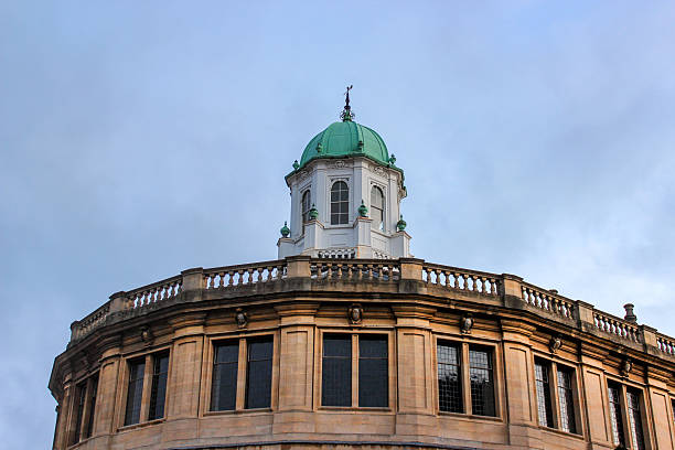 Oxford, United Kingdom - Dec 22, 2025: A close-up of the octagonal dome with a green finial on the stone building of the Sheldonian Theatre in Oxford against a cloudy sky.