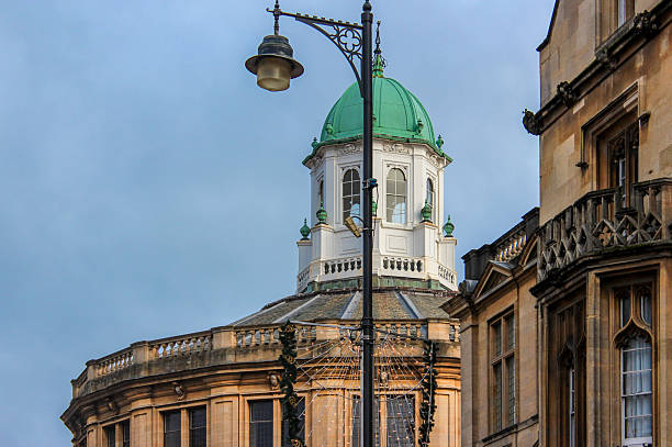 Oxford, United Kingdom - Dec 22, 2025: A close-up of the octagonal dome with a green finial on the stone building of the Sheldonian Theatre in Oxford against a cloudy sky.
