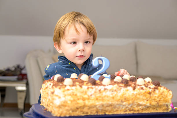A calm toddler looks attentively at a birthday cake with a blue number candle during a quiet indoor family celebration.