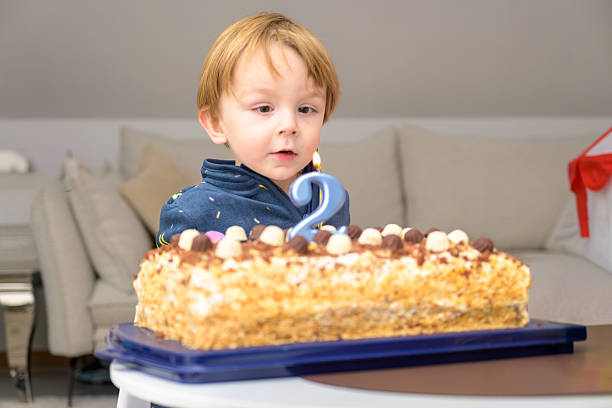 A young toddler looks curiously at a lit number candle on a birthday cake during a cozy indoor family celebration.