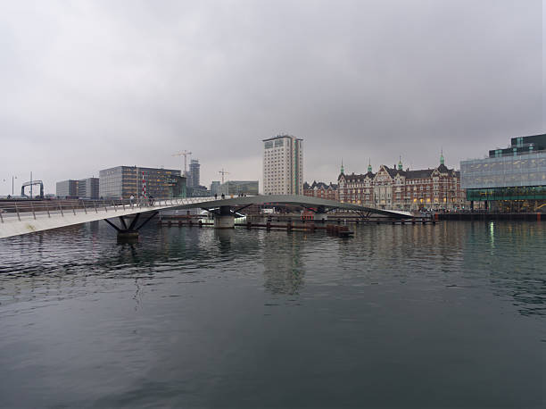 Modern Lille Langebro pedestrian bridge spanning calm water with urban skyline and historic buildings reflected, Copenhagen, Denmark