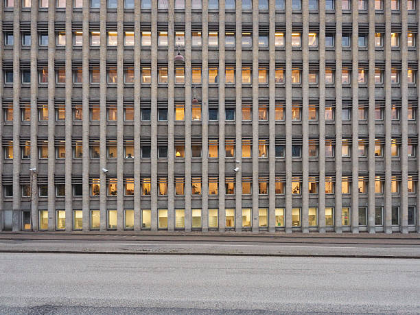 Contemporary office building with illuminated windows and people walking on sidewalk at dusk