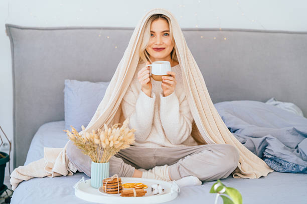 istock Thoughtful cozy woman drinking cocoa under blanket on bed at home 2255590256