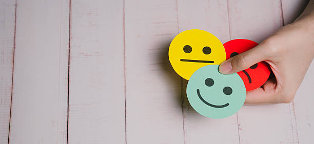 istock Feedback concept. Hand holding colorful paper cutout smiley faces showing different emotions on wooden background, positive and negative feelings concept 2255592318