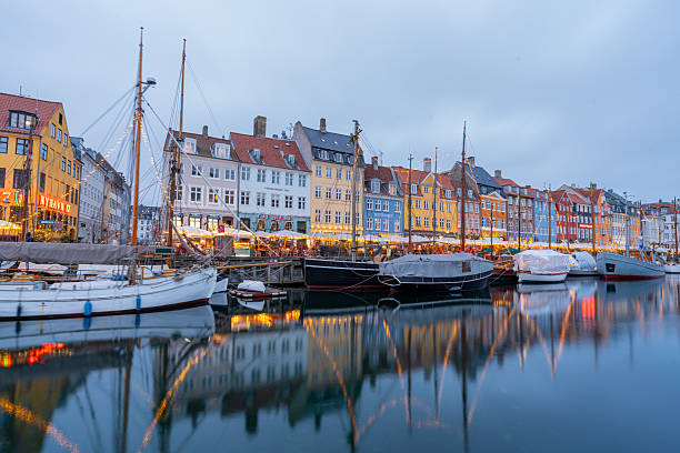 Nyhavn, Copenhagen, Denmark – Colorful waterfront buildings and illuminated restaurants reflecting on the canal at blue hour, with historic sailboats moored along the harbor.