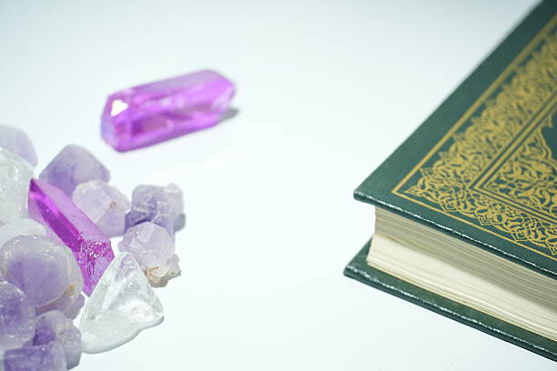 This serene image beautifully combines spiritual elements with the natural beauty of crystals, featuring a Quran and an assortment of purple and clear stones on a white surface.