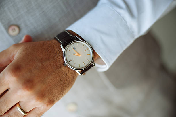 A man is wearing a black suit and is looking at his watch. The watch is black and has a silver band. The man is in a hurry or is checking the time.