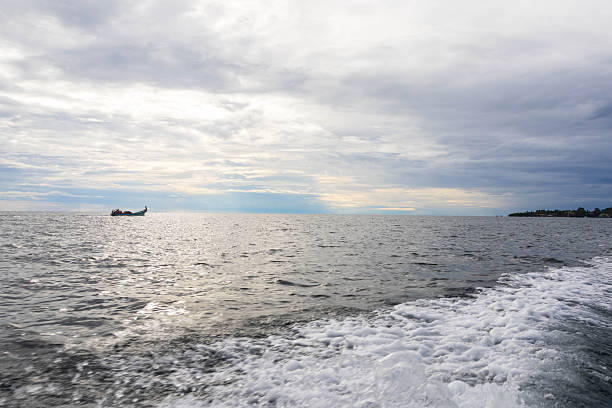 Wide view of open sea with a small boat in the distance beneath a cloudy sky, capturing a calm coastal atmosphere and sense of space.