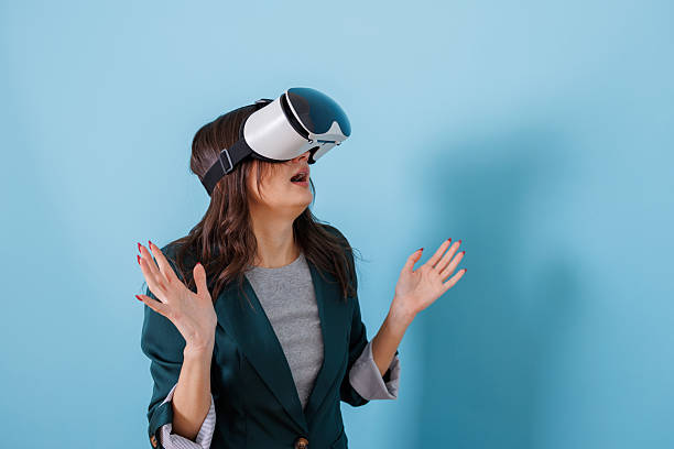 Woman wearing vr headset on a blue background, expressing surprise and wonder while interacting with virtual content