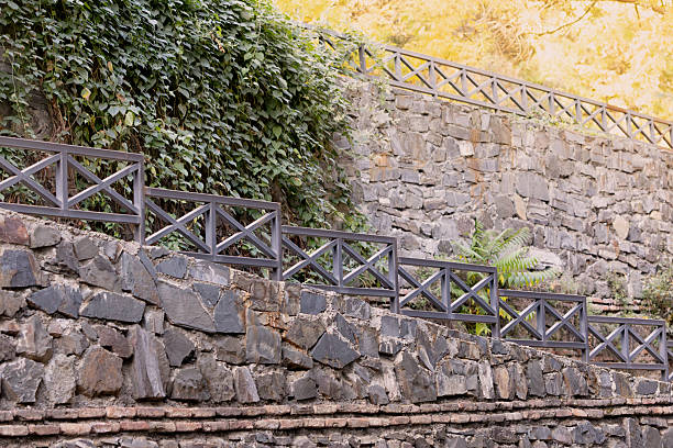 Iron railing running along a rustic stone wall with green ivy covering the background, creating a natural architectural garden element