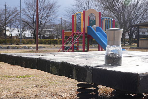 A playground with a slide and a swing set. A jar is sitting on a wooden bench