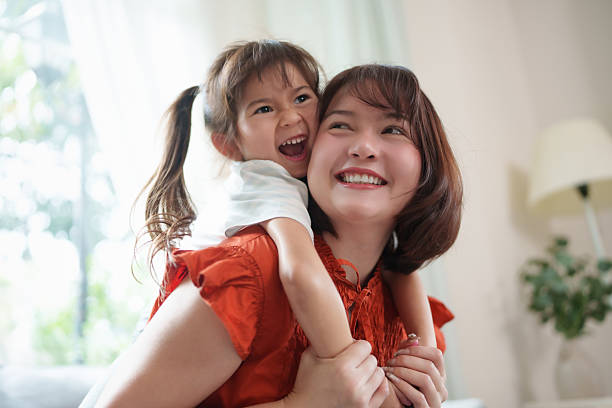 Asian mother enjoying a sweet hug from her young daughter indoors. family, happiness, affection, and close relationship.