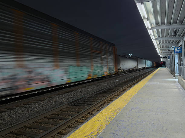 Frieght train in motion passing by Lombard, Illinois  Metra station platform at night.