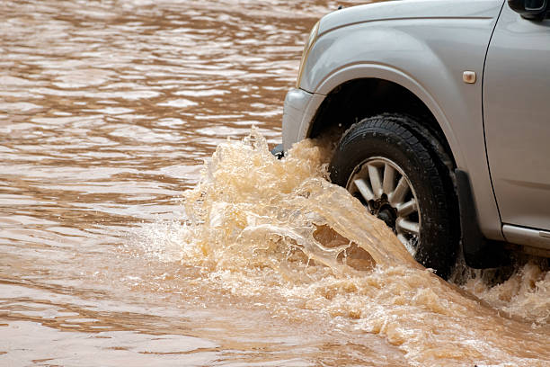 Dark yellow floodwater covers a rural road, hindering commuters. Environmental issues such as global warming, natural disasters, and the impacts of deforestation can affect car insurance policies.