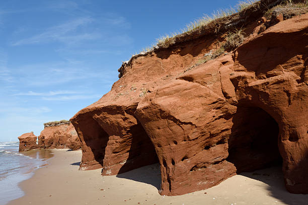 Red sandstone caves formed by erosion on an island coastline with beach and cliffs on a summer day (Pointe-aux-Loup, Iles de la madeleine)