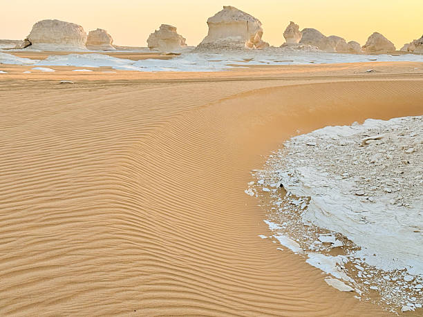 Soft morning light over rippled sand and distant chalk formations in Sahara desert