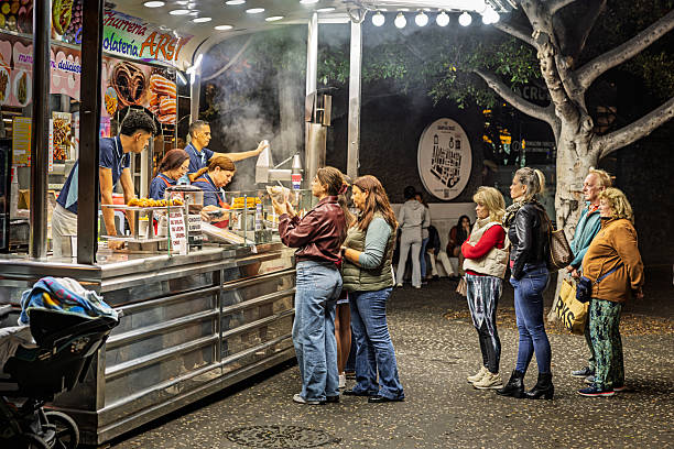 Santa Cruz, Tenerife, Spain, Europe - December 21th 2025: A line of people stands in an orderly queue in front of a busy fast‑food stall staffed by four workers at the annual Christmas market in the middle of the city. The scene shows everyday visitor activity at the seasonal event