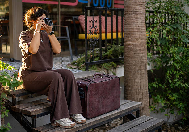 Young woman photographing with a vintage camera during golden hour with travel suitcase