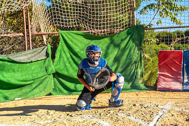 Young baseball player wearing catcher’s mask and chest protector, holding a mitt