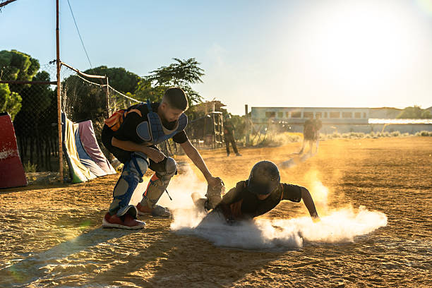 Young Caucasian male catcher energetically tags a runner sliding into home plate on a sunny baseball field featuring vibrant green surroundings and a clear blue sky.