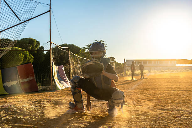 A determined teen in a catchers helmet stands ready on the field for the pitch