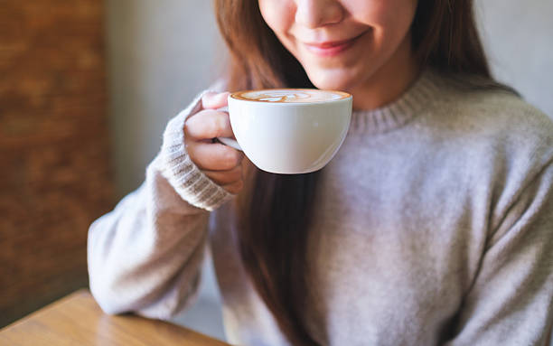 Closeup image of a woman holding and drinking hot latte coffee