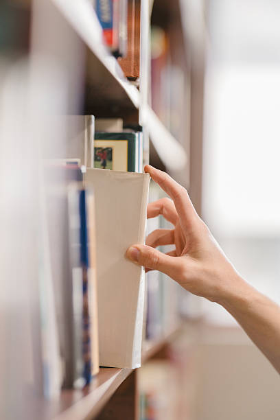 istock right hand choosing and picking book in public library. 2255653460