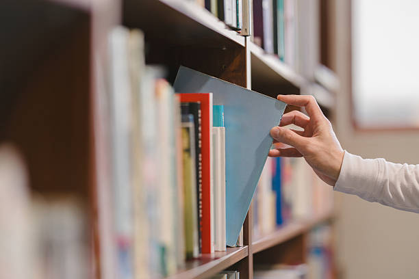istock right hand choosing and picking book in public library. 2255653524