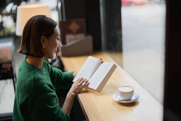 A young woman of Korean origin sits in the library by the window and reads a book