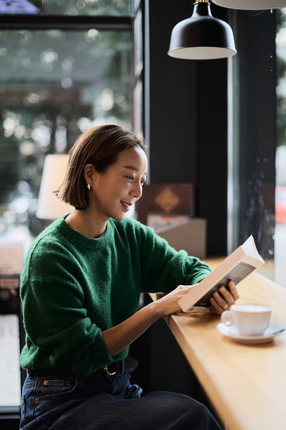 A young woman of Korean origin sits in the library by the window and reads a book