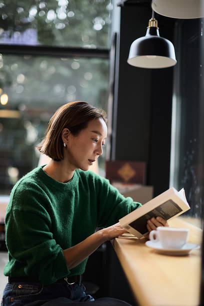 A young woman of Korean origin sits in the library by the window and reads a book