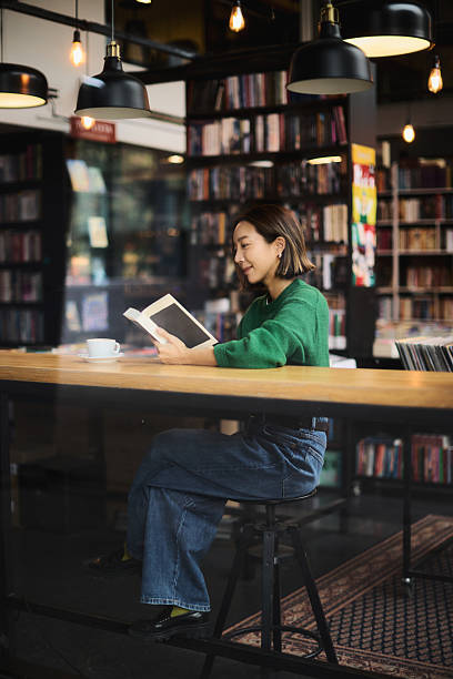 A young woman of Korean origin sits in the library by the window and reads a book