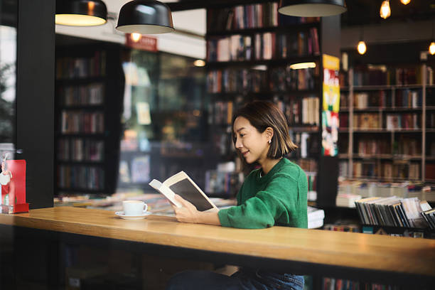 A young woman of Korean origin sits in the library by the window and reads a book