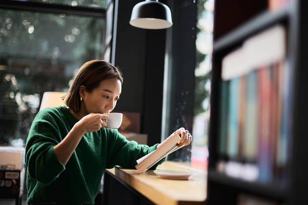 A young Korean woman is drinking coffee while reading a book in the library