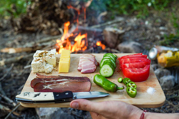 Camping preparation scene featuring boiling water being poured into noodles in an outdoor setting. Includes hiking and cooking gear, promoting wilderness exploration and outdoor meals.