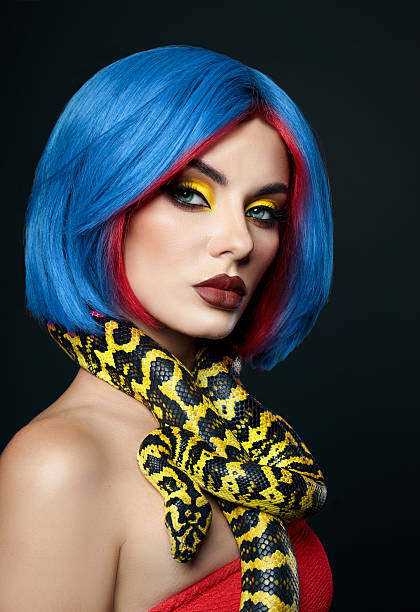 A vibrant close-up portrait featuring a smiling woman with striking blue eyes and a sleek black bob. She wears a denim jacket against a bold red backdrop, conveying a playful yet stylish mood. The image highlights clear skin, expressive eyes, and a friendly, approachable vibe suitable for fashion, lifestyle, and beauty themes.
