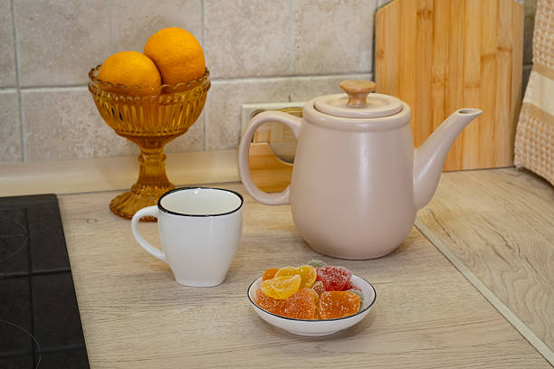 Warm tea and colorful sweets on a kitchen counter with fresh fruit nearby.